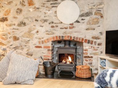 A stone wall with a wood burning stove fireplace cushions bucket and basket at Ty ar Ben Bryn in Pencarnisiog near Rhosneigr