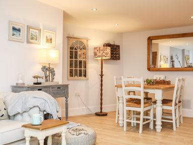 A dining area with a wooden table and white chairs next to a living space with a sofa table and lamps at Ty ar Ben Bryn Pencarnisiog near Rhosneigr
