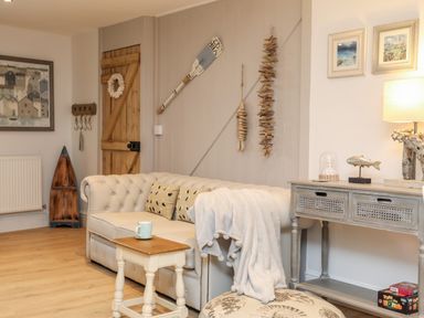 A living room with a beige sofa and wooden door with coastal decor at Ty ar Ben Bryn in Pencarnisiog near Rhosneigr
