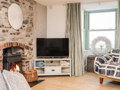 A living room with a wood-burning stove a television on a white stand and a window with light green curtains at Ty ar Ben Bryn in Pencarnisiog near Rhosneigr
