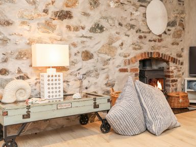 A living room with a stone wall wood stove coffee table with lamp and large cushions on the floor at Ty ar Ben Bryn in Pencarnisiog near Rhosneigr