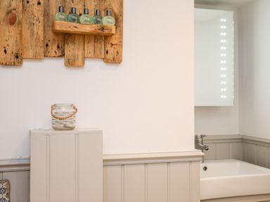 A bathroom with a sink faucet a mirror a wooden wall shelf with toiletries and a glass jar on a white painted cabinet at Ty ar Ben Bryn in Pencarnisiog near Rhosneigr