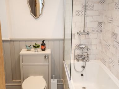A bathroom with a toilet, a small cabinet, a bathtub with shower fixtures, and a decorative mirror at Ty ar Ben Bryn in Pencarnisiog near Rhosneigr
