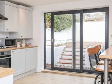 A kitchen with white cabinets wooden countertops a microwave glass sliding door and wooden chairs at Ty ar Ben Bryn Pencarnisiog near Rhosneigr