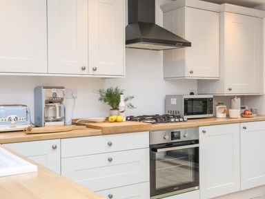 A kitchen with white cabinets wooden countertops a blue toaster a coffee maker a gas stove an oven a microwave and kitchen items on the counter at Ty ar Ben Bryn in Pencarnisiog near Rhosneigr