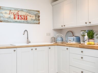 A kitchen with white cabinets wooden countertops a stainless steel faucet blue kettle toaster plants and a fresh fish sign at Ty ar Ben Bryn in Pencarnisiog near Rhosneigr