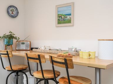 A kitchen counter with three wooden stools cups a bread container macarons a teapot and a radio at Ty ar Ben Bryn in Pencarnisiog near Rhosneigr