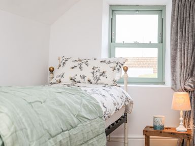 A bedroom with a bed near a window and a wooden bedside table with a lamp and candle at Ty ar Ben Bryn in Pencarnisiog near Rhosneigr