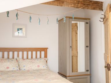 A bedroom with a wooden bed, patterned bedding, a wardrobe with a mirrored door, fish decorations hanging on a string, and a wooden beam at Ty ar Ben Bryn in Pencarnisiog near Rhosneigr