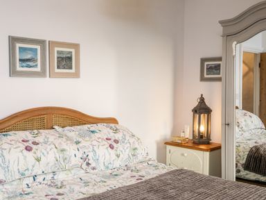 A bedroom with floral bedding a wooden headboard a nightstand with a lantern lamp and a mirror wardrobe at Ty ar Ben Bryn in Pencarnisiog near Rhosneigr