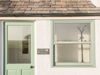 A mint green door and window on a white exterior wall with a coat rack visible inside at Ty ar Ben Bryn in Pencarnisiog near Rhosneigr