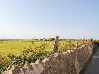 A rural landscape with a stone wall and barbed wire fence alongside a road at Ty ar Ben Bryn in Pencarnisiog near Rhosneigr