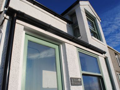 Exterior of a white textured building with green window frames and a black drainpipe at Ty ar Ben Bryn in Pencarnisiog near Rhosneigr