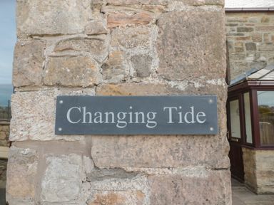 A stone wall with a sign reading Changing Tide at Changing Tide in Beadnell