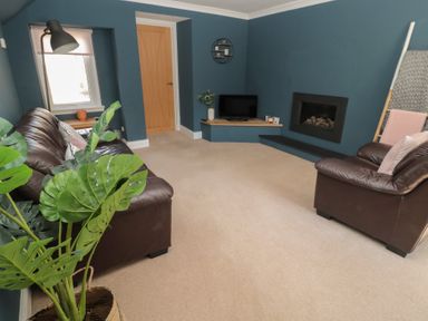 A living room with brown leather sofas a TV on a corner shelf and a fireplace at Changing Tide in Beadnell