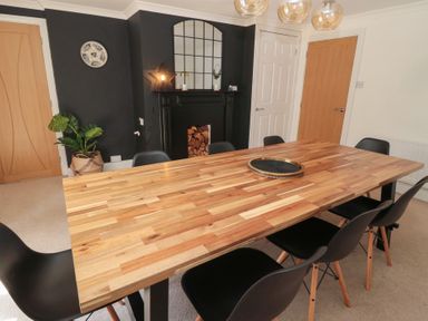 A dining room with a wooden table surrounded by black chairs and a black fireplace with a mirror above it at Changing Tide in Beadnell