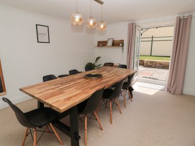 A dining room with a wooden table surrounded by black chairs and a door open to a garden at Changing Tide in Beadnell