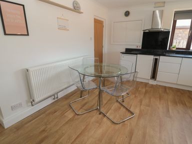 A kitchen with a round glass table and four transparent chairs near a radiator and white cabinets at Changing Tide in Beadnell
