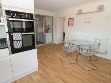 A kitchen with built in ovens and a glass dining table with four transparent chairs at Changing Tide in Beadnell
