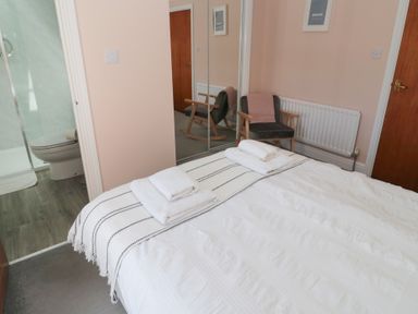 A bedroom with a bed and folded towels a chair and an en suite bathroom at Changing Tide in Beadnell