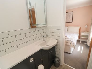 A bathroom with a sink and mirror cabinet next to a bedroom with a bed and nightstand at Changing Tide in Beadnell