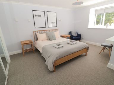 A bedroom with a wooden bed a gray blanket two towels two framed wall arts above the bed a blue armchair and a window at Changing Tide Beadnell