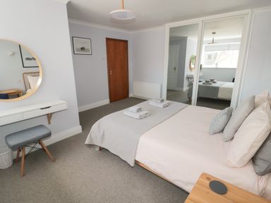 A bedroom with a bed folded towels and pillows a wooden door a mirrored wardrobe a wall mirror and a gray stool at Changing Tide in Beadnell