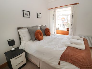 A bedroom with a double bed with white bedding orange and gray cushions beside a nightstand with a lamp at Changing Tide in Beadnell