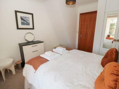A bedroom with a bed with orange cushions white towels a dresser and a wooden door at Changing Tide in Beadnell