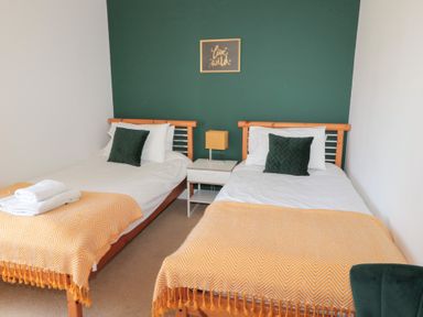 A bedroom with two single beds with yellow throws and green pillows at Changing Tide in Beadnell