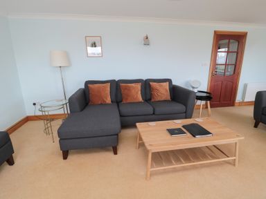 A living room with a gray sofa with brown cushions a wooden coffee table and a glass side table at Changing Tide in Beadnell