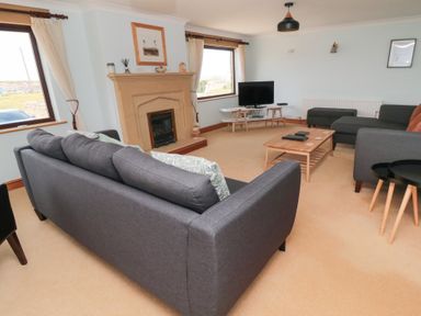 A living room with grey sofas a wooden coffee table a fireplace and a television at Changing Tide in Beadnell