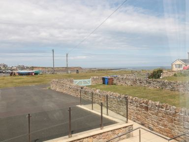 An outdoor view of a stone wall yard with grass bins boats and a sea horizon at Changing Tide in Beadnell