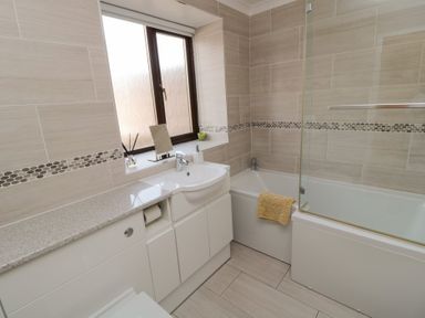 A bathroom with a bathtub a sink white cabinets and a window at Changing Tide in Beadnell