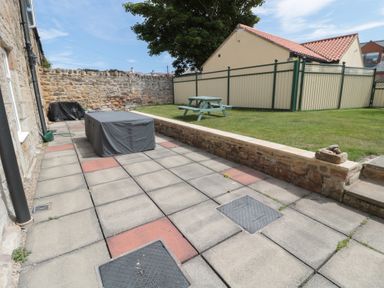 A garden patio with covered furniture a stone wall and a wooden picnic table on the grass at Changing Tide in Beadnell