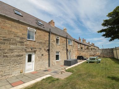 A stone house with multiple windows and doors facing a garden with a picnic table and covered outdoor furniture at Changing Tide in Beadnell