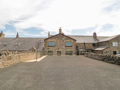 A stone building with multiple windows and chimneys surrounded by stone walls at Changing Tide in Beadnell