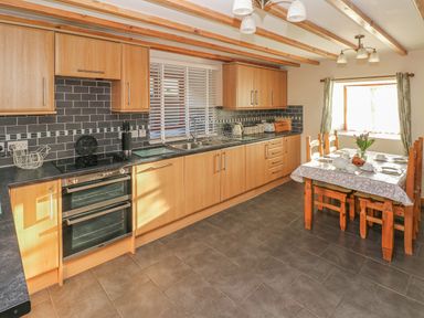 A kitchen with wooden cabinets, a black countertop, a dining table set with dishes and flowers at Little Brook Cottage in Laugharne