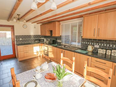 A kitchen with wooden cabinets a dining table with tulips and a cake at Little Brook Cottage in Laugharne