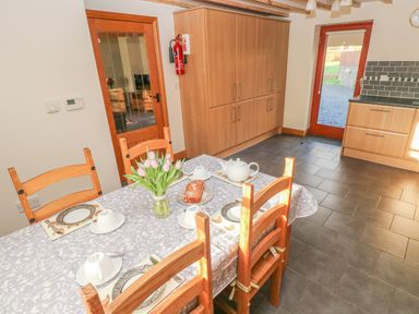 A kitchen with a dining table set for tea with tulips in a vase a cake and wooden chairs at Little Brook Cottage in Laugharne