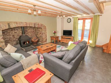 A living room with two gray sofas a wooden coffee table stone fireplace and glass doors with green curtains at Little Brook Cottage in Laugharne