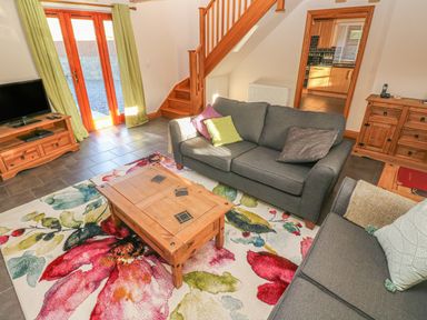 A living room with two gray sofas a wooden coffee table a floral rug a wooden cabinet a TV on a wooden stand and stairs leading upstairs at Little Brook Cottage in Laugharne