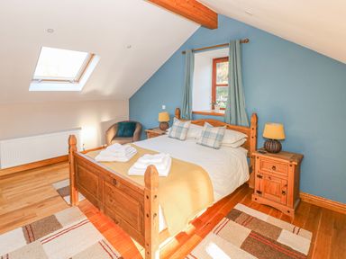 A bedroom with a wooden bed with folded towels bedside tables lamps a chair and a skylight window at Little Brook Cottage in Laugharne