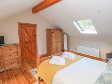 A bedroom with a wooden bed folded towels wooden wardrobe chest of drawers door and skylight window at Little Brook Cottage in Laugharne