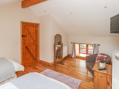 A bedroom with wooden floor a wooden door a small window an armchair a wooden cabinet and a standing mirror at Little Brook Cottage in Laugharne