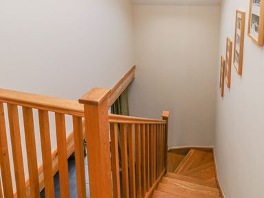A wooden staircase with vertical railings and framed pictures on the wall at Little Brook Cottage in Laugharne