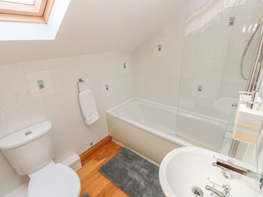 A bathroom with a toilet a bathtub a sink a towel on a rack and a skylight window at Little Brook Cottage in Laugharne