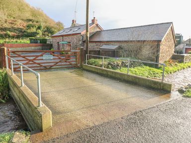 A gated driveway with a stone house and grassy area behind at Little Brook Cottage in Laugharne