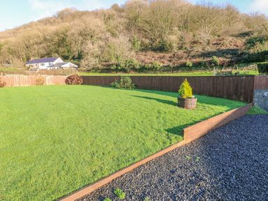 A grassy garden area with a wooden fence and a potted plant next to a gravel path at Little Brook Cottage in Laugharne