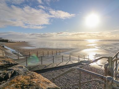 A beach with a rocky foreground railing and a chain fence near the shore at Little Brook Cottage in Laugharne